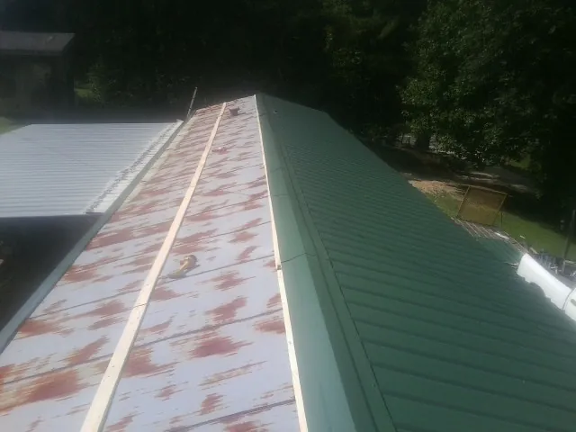 Old rusted panels beside newly installed green metal roofing — Wind Damage Roof Repair by Roofing Brothers in Baldwin