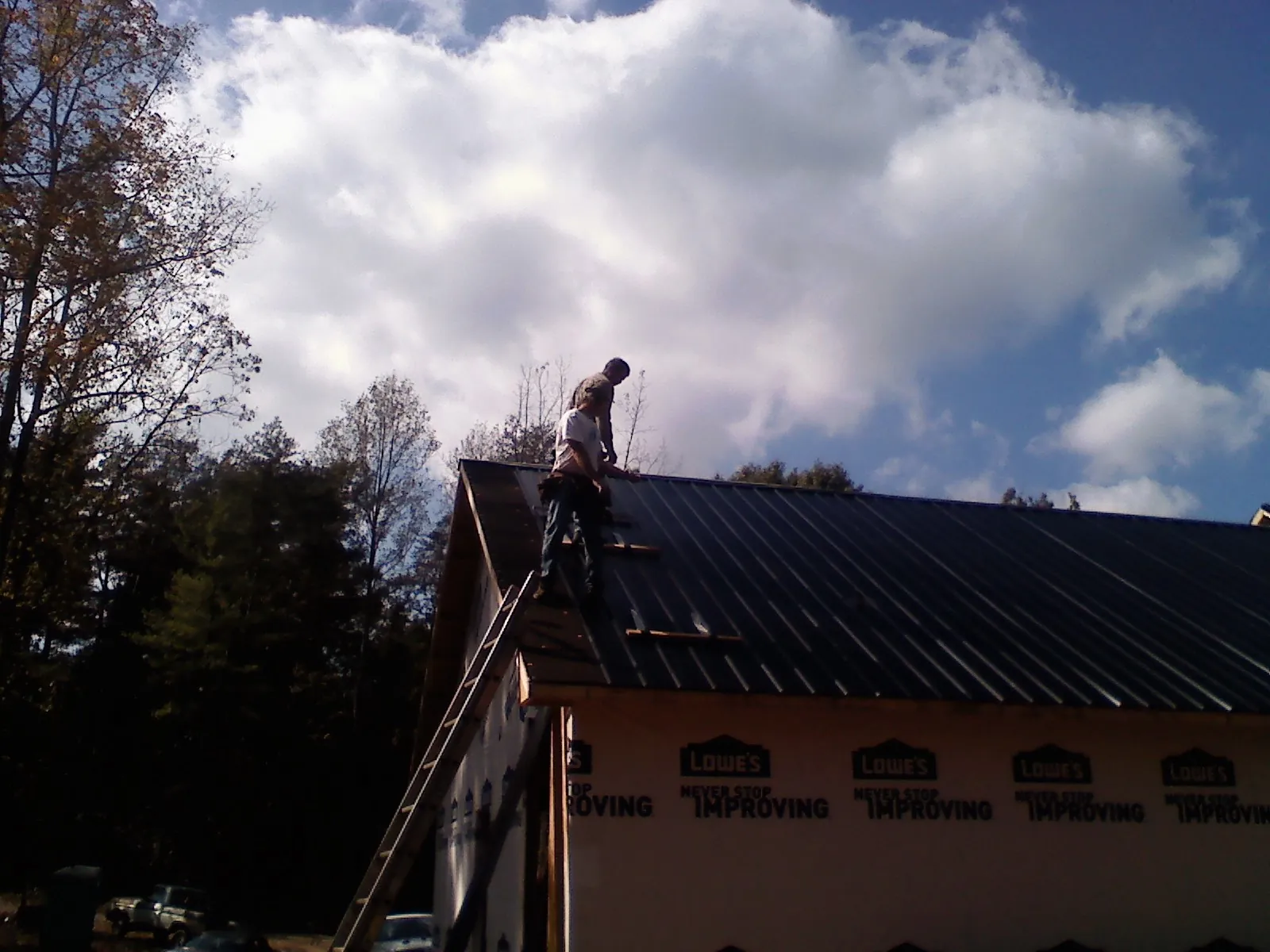 Roofer fastening dark metal panels high against a cloudy sky, from a Roof Inspection job in Baldwin