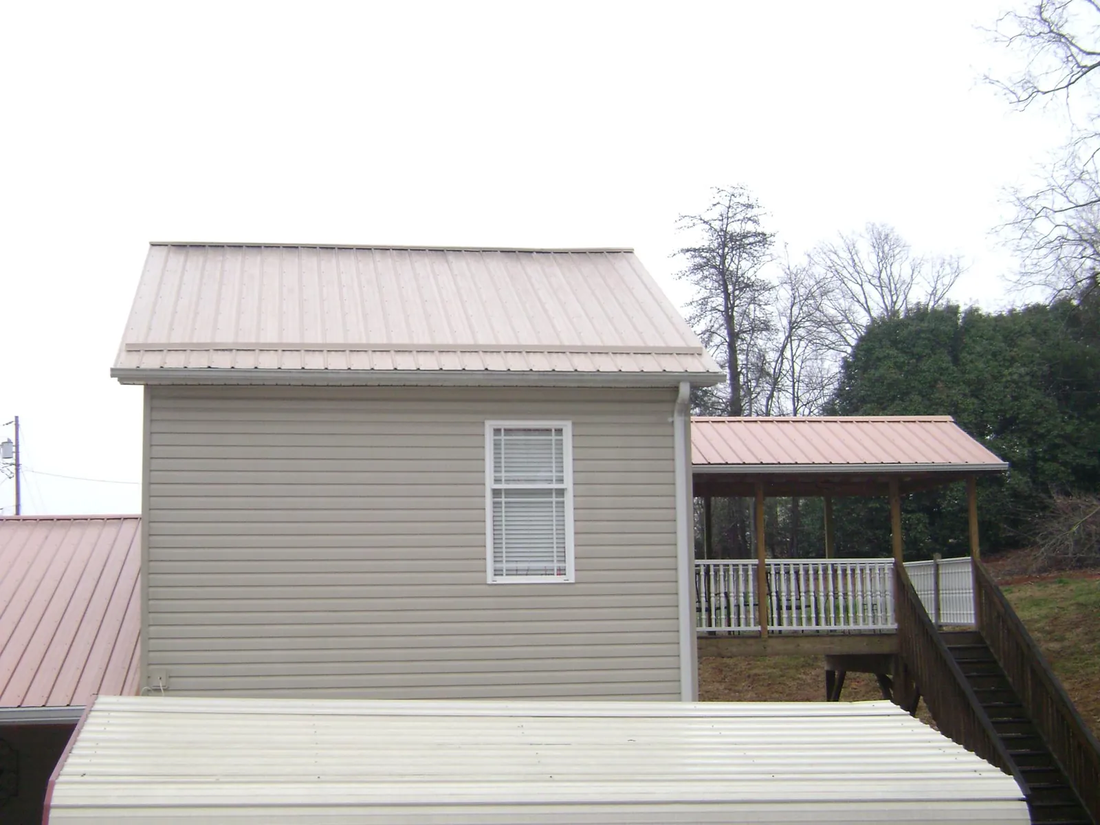 Tan metal roofs on a two story addition and attached porch, from a Roof Replacement job in Baldwin