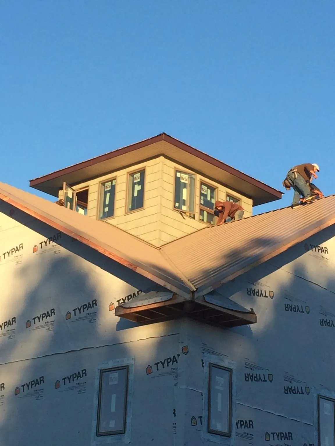 Roofers working around a rooftop cupola on a new metal roof at sunset — Roof Waterproofing in Baldwin by Roofing Brothers